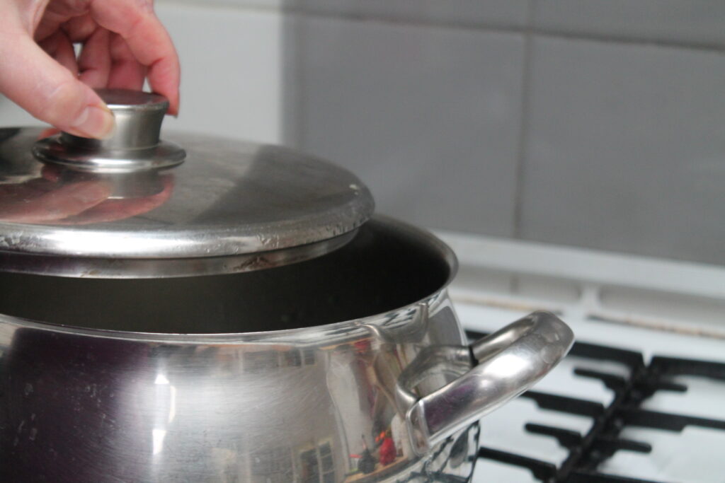 Pan on stove with lid being opened. What is inside? Is the food being cooked properly?