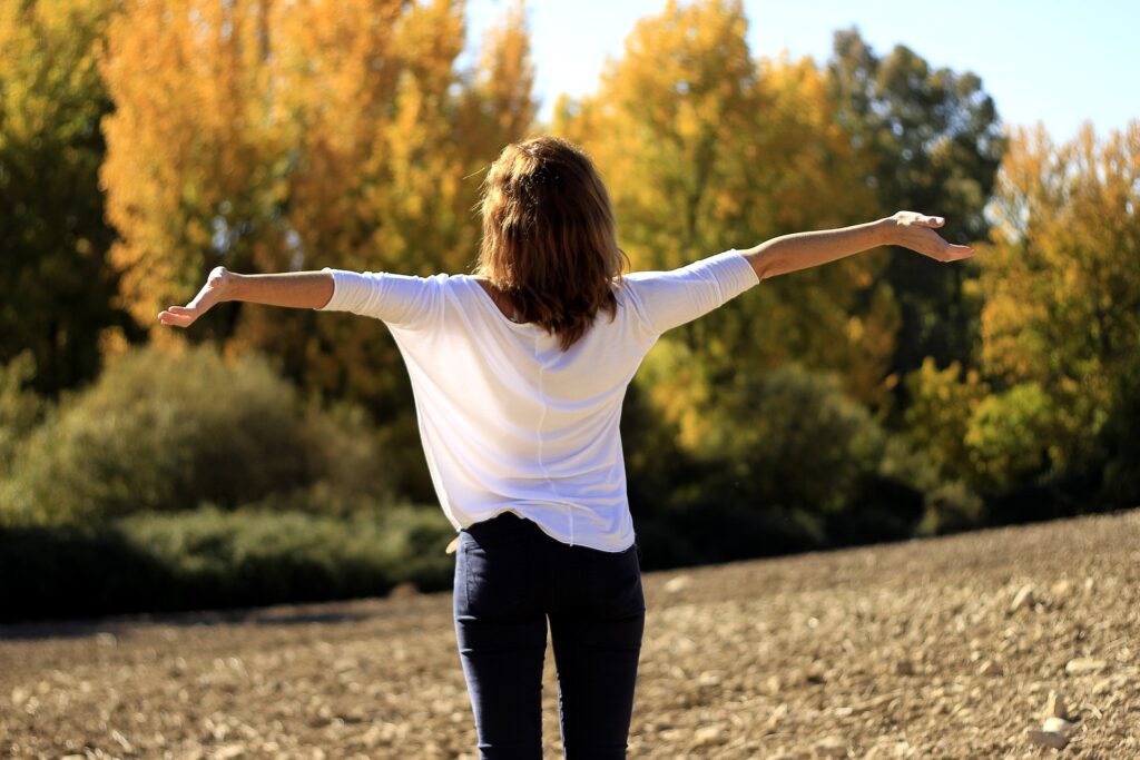 Woman greeting the sun with wide arms. Being outdoors and enjoy nature is important for my self care.