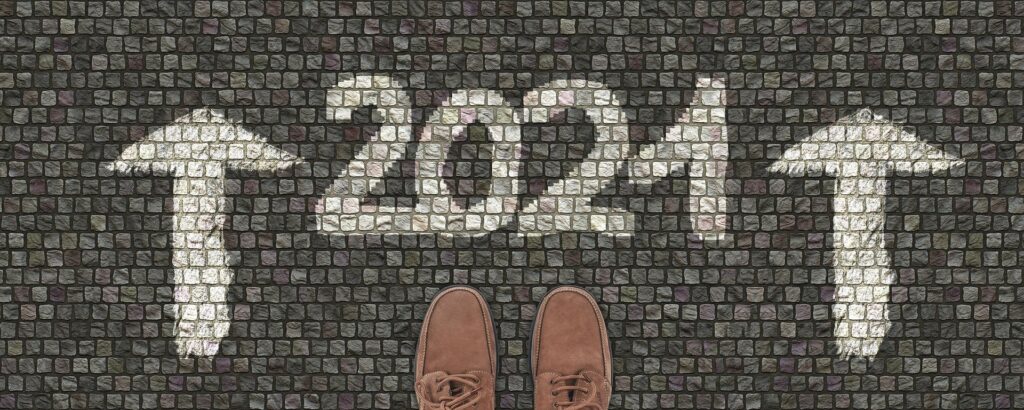 2021 written on paving with two arrows facing forward. Two shoes are lined up ready to enter into 2021.